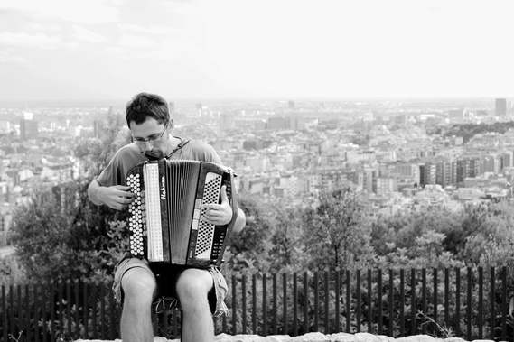 A black and white landscape oriented portrait fine art photo of a local Spanish musician man playing an accordion at Park Guell in Barcelona 