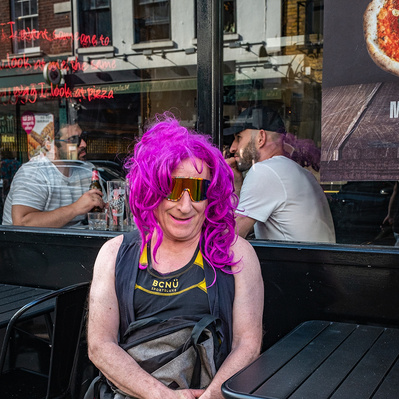 A man with a pink weak sitting outside a bar colour photography