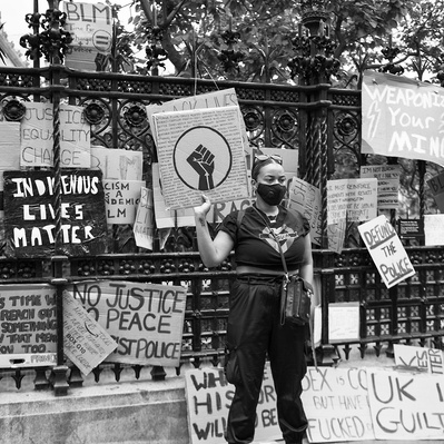 'Woman holding a banner outside houses of parliament at the Black Lives Matter Protests, Black and White London Street Photography'