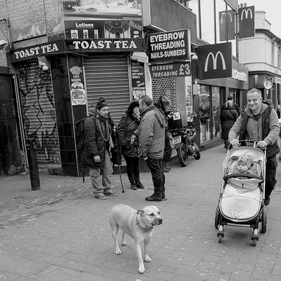 A man with a baby in a pram and his dog Tooting Broadway south London black-and-white photography