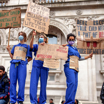 'Three NHS staff standing on a wall in Whitehall holding protest placards at the Black Lives Matter Protests, London Colour Street Photography'