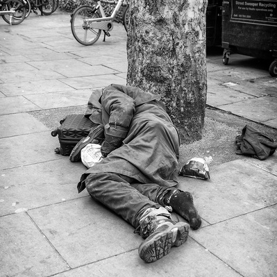 A rough sleeper sleeping on the ground with one shoe off London black-and-white photography