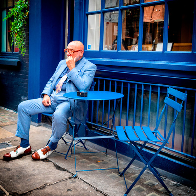 Man sitting outside a coffee shop dressed in Blue Soho London colour photography