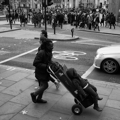 'A father pushing his son tied to a luggage trolly'
