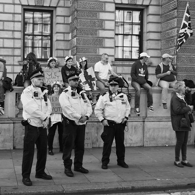 'Pro Brexit Protester sitting on a wall with met police officers standing in front, London Black and White Street Photography'