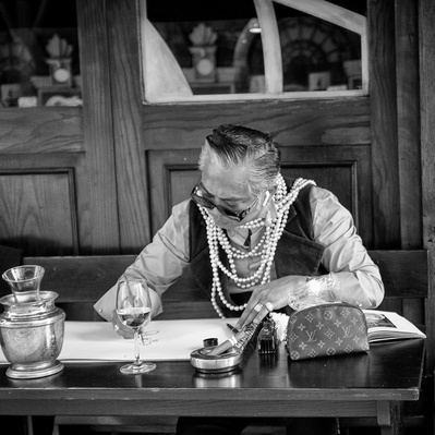A flamboyant dressed man sitting at a table outside a bar, Soho, London black-and-white photo