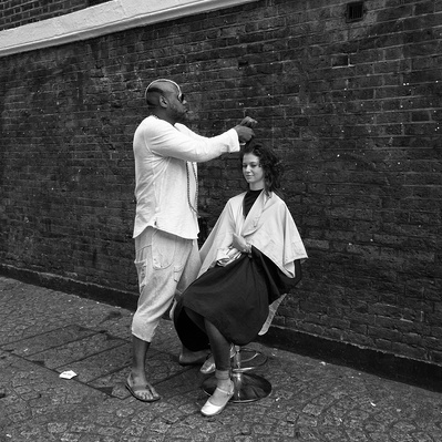 'Hairdresser cutting a womans hair outside in the street, Black & White London Street Photography'