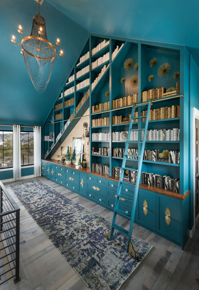 A custom teal library wall with a gold chandelier and teal slide ladder.