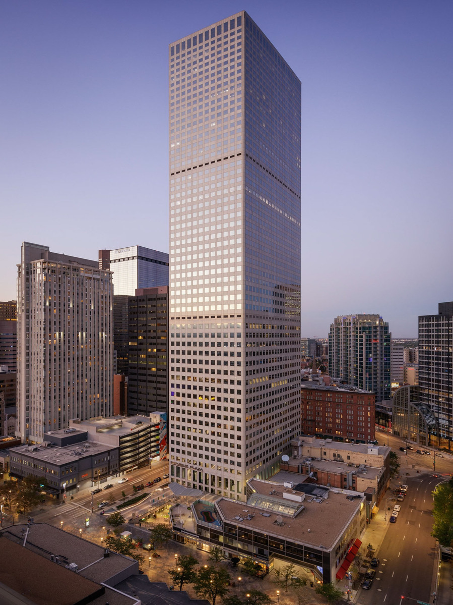 A high rise building in Denver towering over the neighboring buildings in a purple sky at dusk.