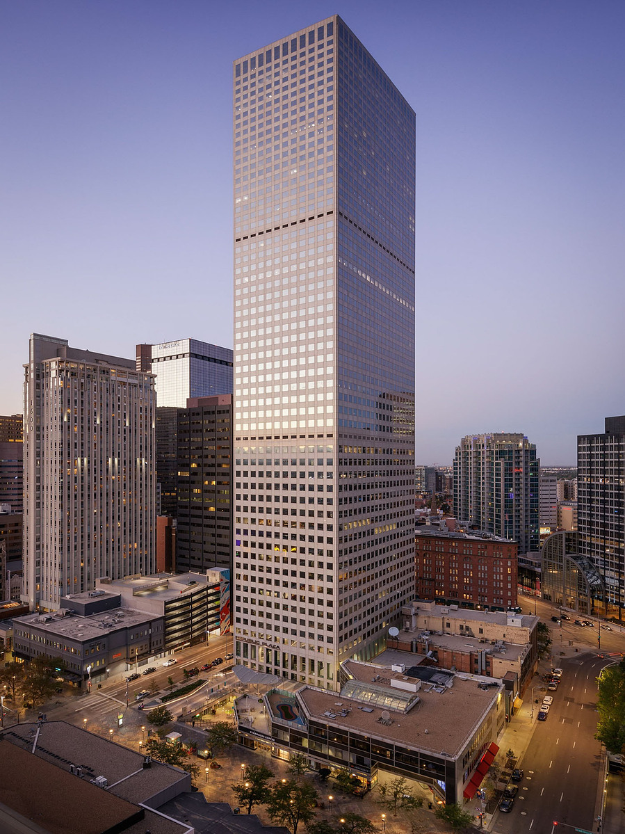 A high rise building in Denver towering over the neighboring buildings in a purple sky at dusk.