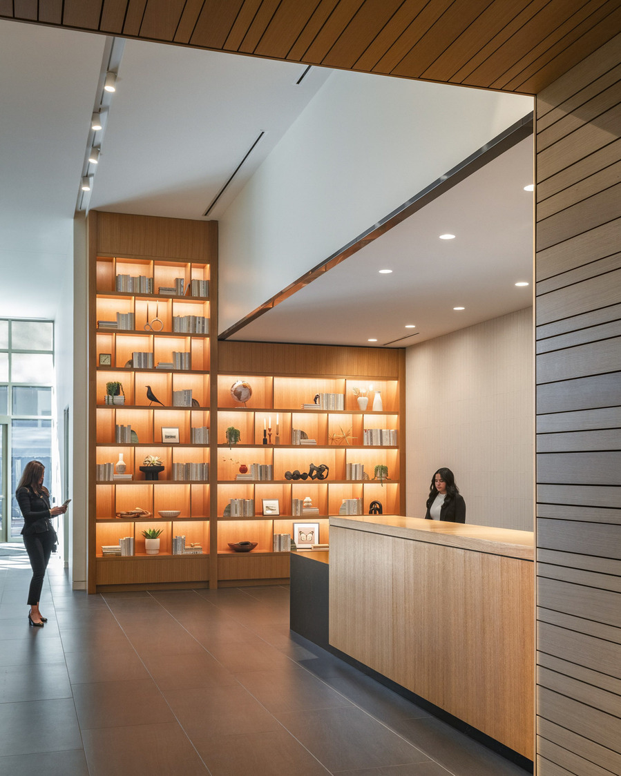 A modern front desk with a large wall with built in shelves that light up with books.
