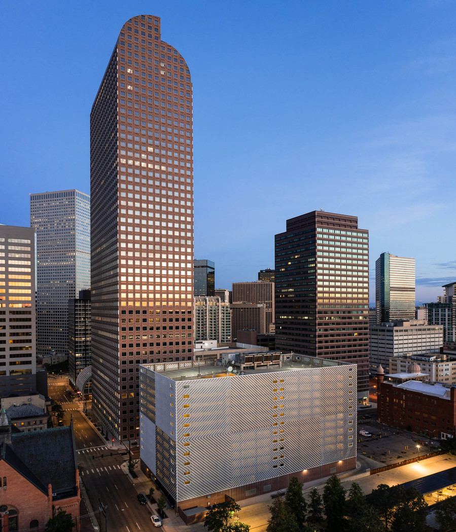 A modern high rise building in downtown Denver at sunrise with light illuminating the facade.