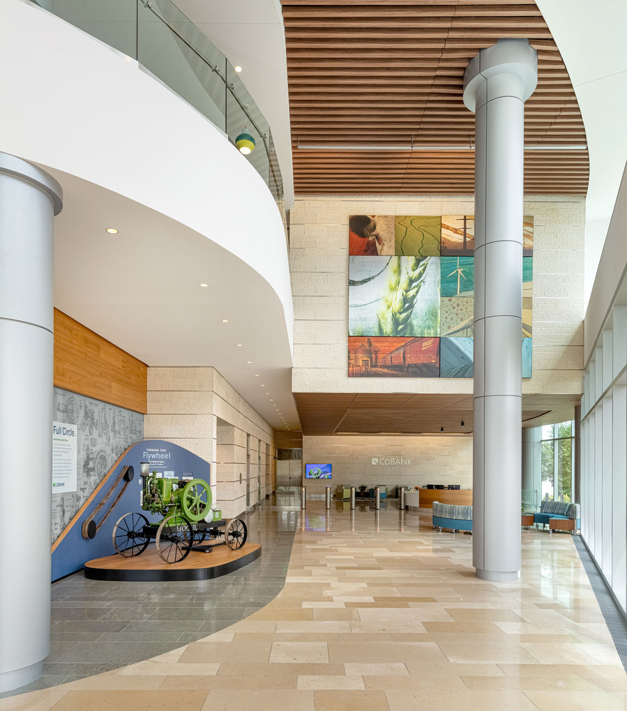 Large bright office lobby with curving lines, wood ceiling, giant pillar and art work.