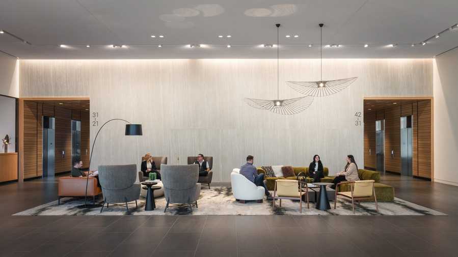 A massive lobby with lots of modern furniture with people sitting and conversing.