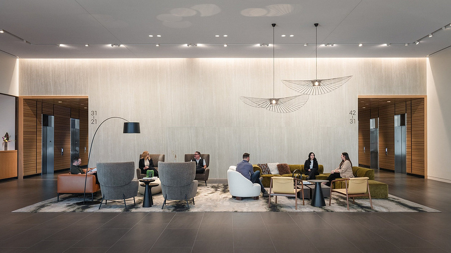A massive lobby with lots of modern furniture with people sitting and conversing.