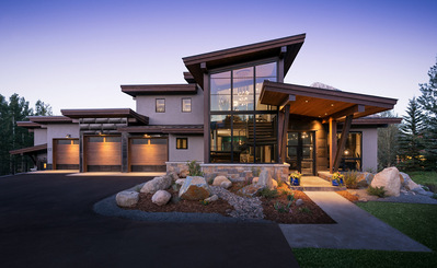 A midcentury modern home with a purple dusk sky and glowing orange lights from the home.