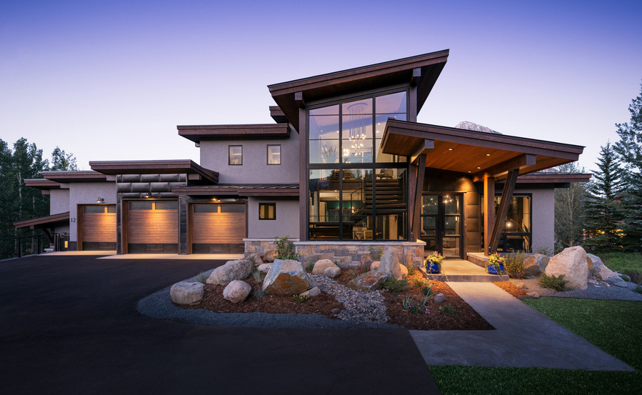 A midcentury modern home with a purple dusk sky and glowing orange lights from the home.