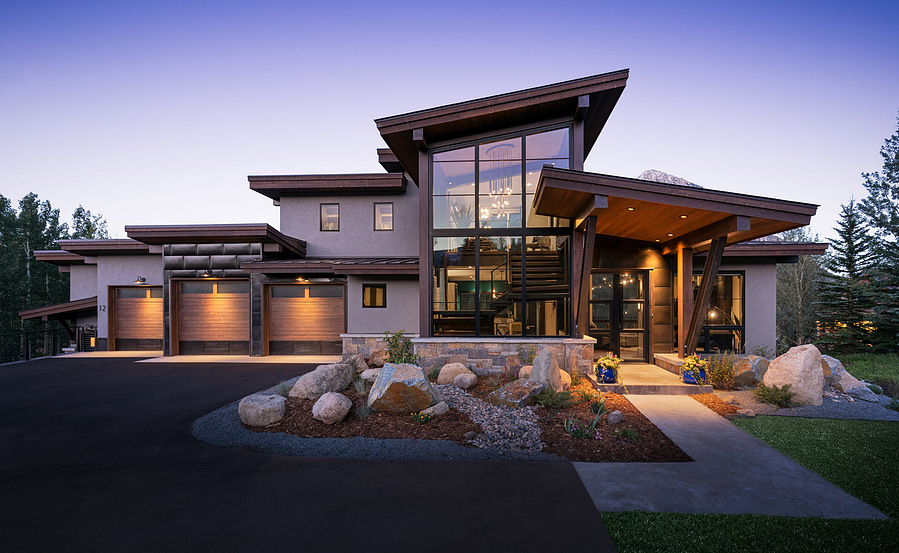 A midcentury modern home with a purple dusk sky and glowing orange lights from the home.