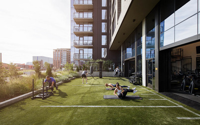 A modern fitness terrace with astroturf in a luxury multifamily building with sun bursting over people working out.