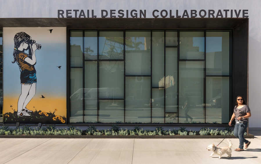 Exterior of a modern office with a mural of a girl taking a photo of a woman walking her dog down the sidewalk.