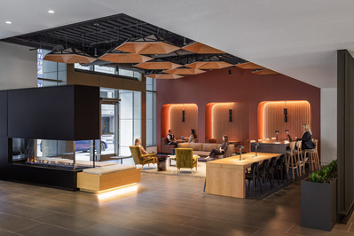 A modern office lobby with a fireplace and red wall with people sitting in the furniture working and conversing