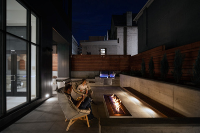 The patio area at Element Marriott Denver, capturing the cozy, outdoor gathering space in a hotel setting with a couple enjoying a drink at the fireplace during dusk.