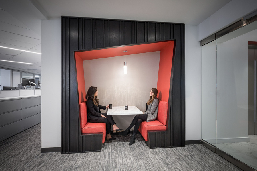 Two women taking a break in a modern red and black wall booth with a table.