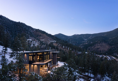 A midcentury modern mountain home during a winter dusk showcasing the building against a snowy landscape.