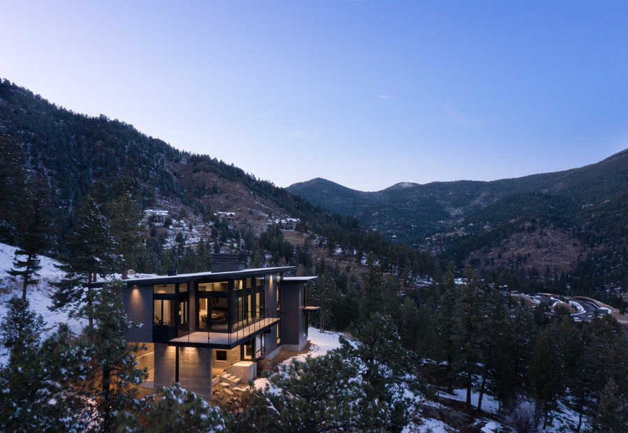 A midcentury modern mountain home during a winter dusk showcasing the building against a snowy landscape.