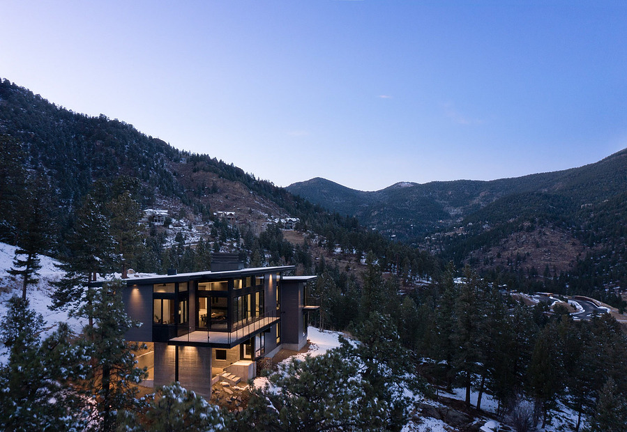 A midcentury modern mountain home during a winter dusk showcasing the building against a snowy landscape.