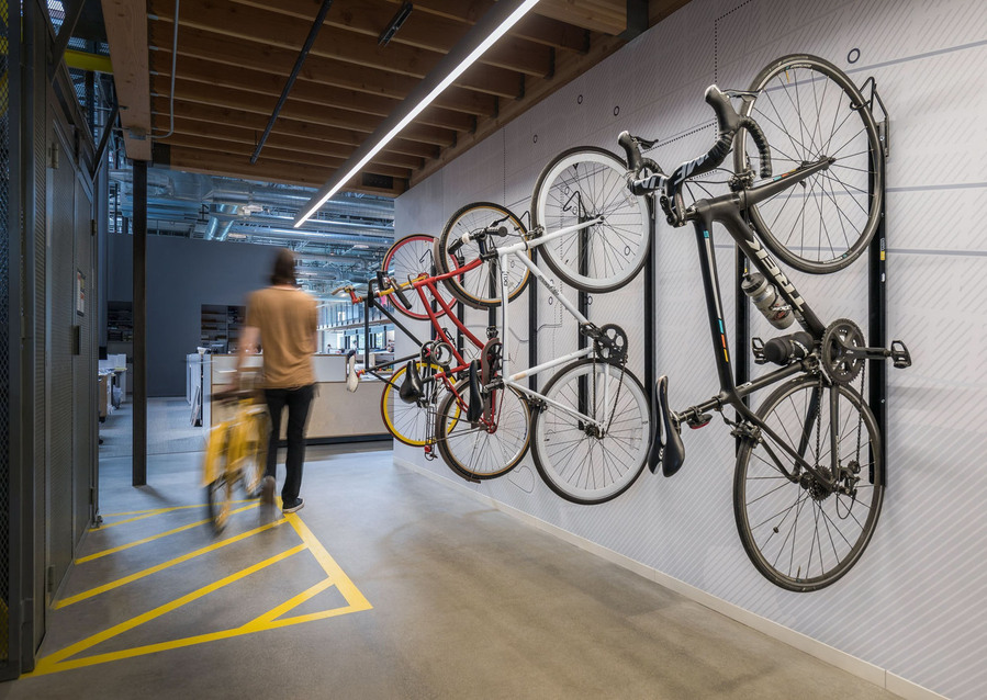 A modern office with a wall bike hanger with 4 bikes and a man in motion walking with a yellow bike.