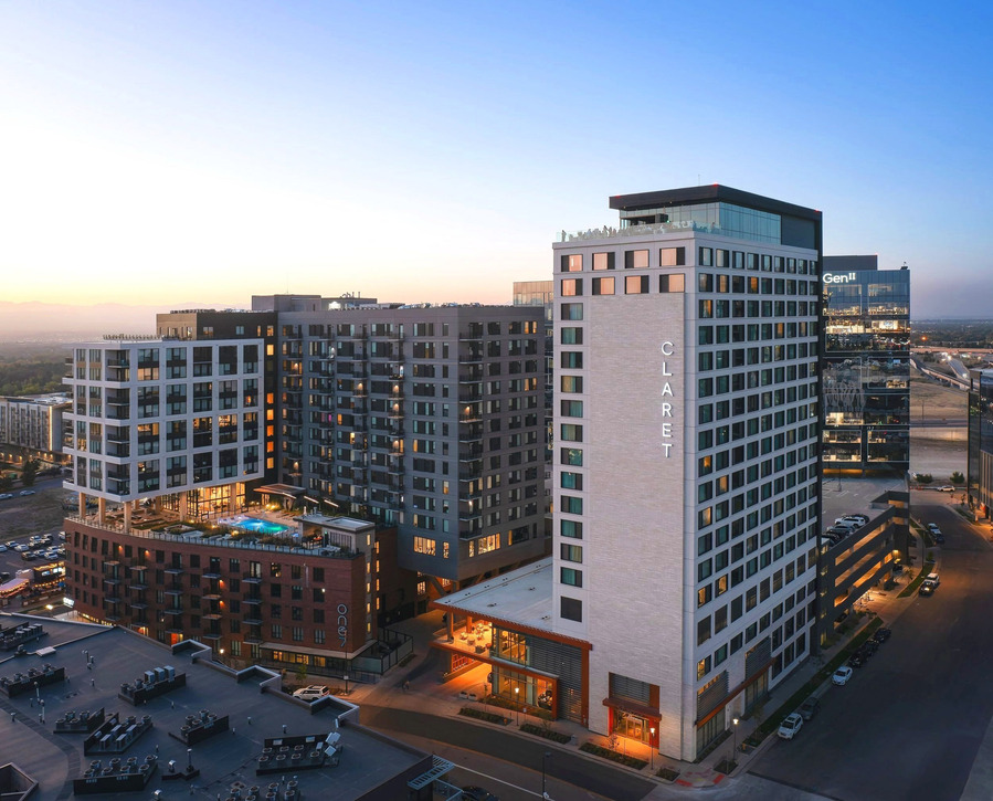 Aerial twilight view of Kimpton Claret Hotel in Denver, showcasing the hotel's exterior illuminated under the evening sky and rooftop bar night life.