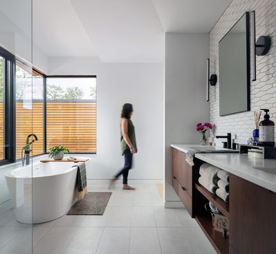 A midcentury modern bathroom with a tub, vanity and woman walking in motion.