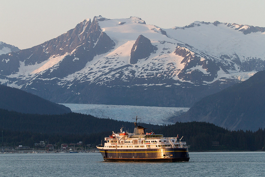Scenic photograph of the marine vessel Taku on the Alaska Marine Highway, with Mendenhall Glacier visible in the background.