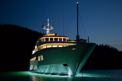 A luxury mega yacht in Alaska on the ocean at night illuminating the surrounding water.