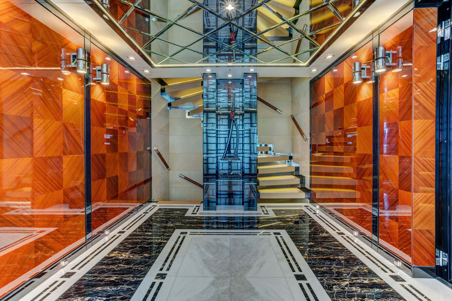A luxury yacht foyer featuring glossy orange walls, mirrored ceiling and a samurai sword center piece if in front of a lit stairwell.