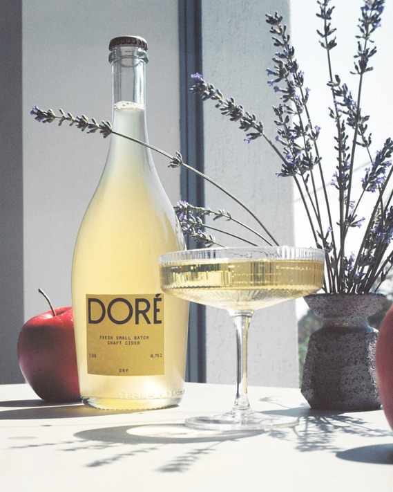 Product photo for Doré Cider, featuring bottles in a minimalist setting under vibrant sunlight. A crisp, natural aesthetic reflecting the essence of premium cider.