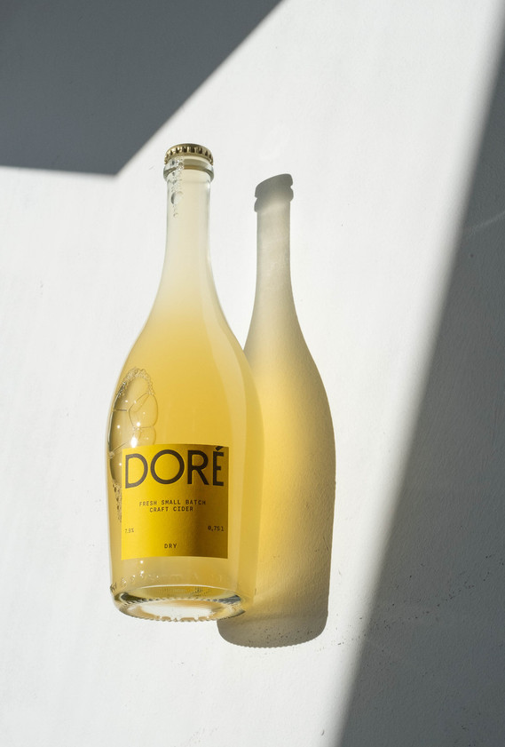 Product photo for Doré Cider, featuring bottles in a minimalist setting under vibrant sunlight. A crisp, natural aesthetic reflecting the essence of premium cider.