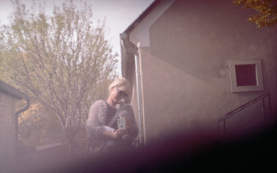 A woman capturing me on her phone as I photograph her—an analog film image exploring layers of observation and mutual creation.