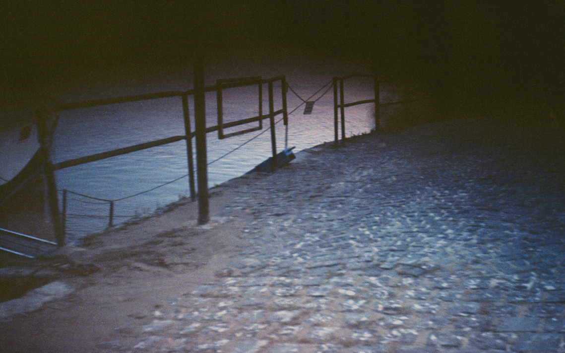 Film photograph capturing a cobblestone riverside of the Danube in the serene glow of post-sunset light.