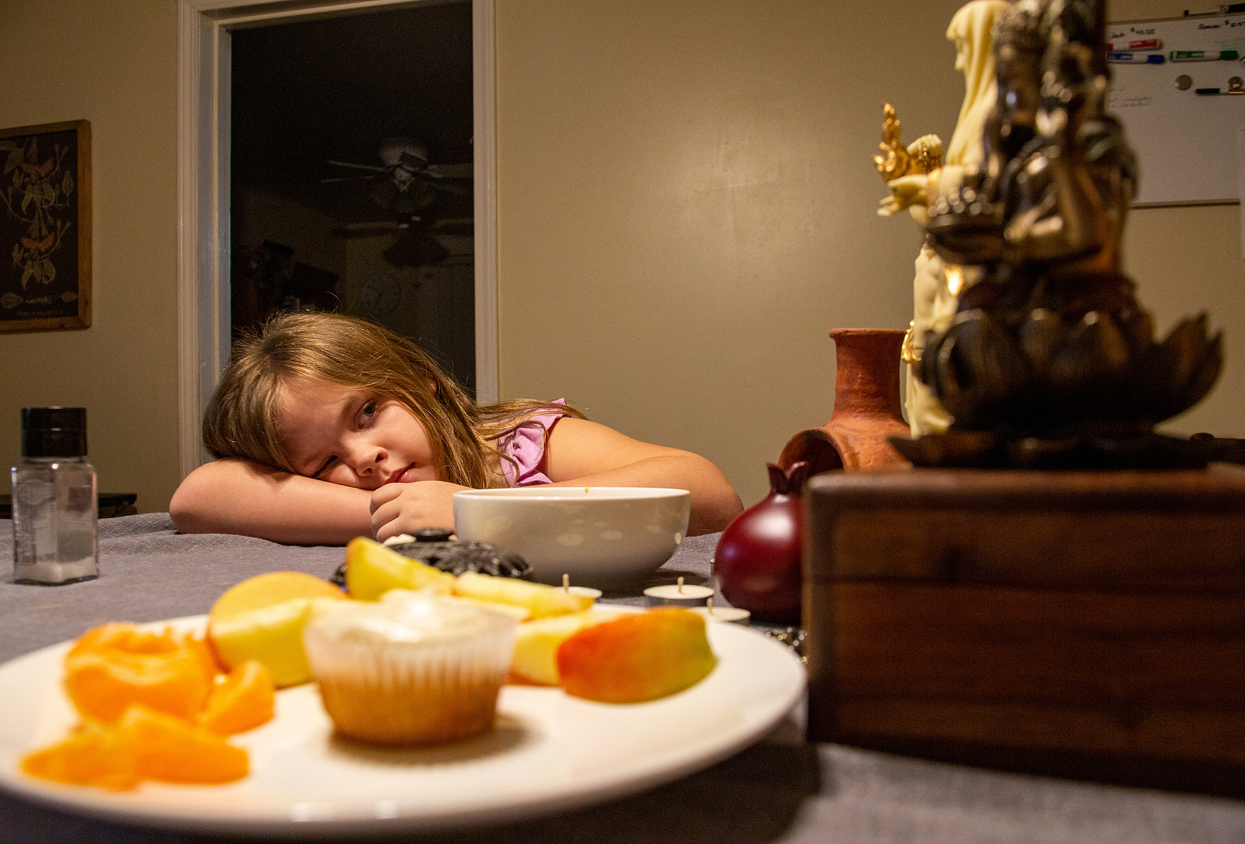 Samantha Williams daughter examines the alter on her dinner table while her mother prepares dinner. An offering to the gods of fruit and a cupcake lays in front of the alter to their house gods, Ganesha, Krishna, Hestia, Dionysos, Hermes, Persephone, and