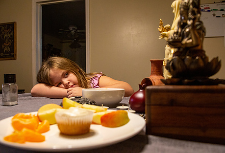 Samantha Williams daughter examines the alter on her dinner table while her mother prepares dinner. An offering to the gods of fruit and a cupcake lays in front of the alter to their house gods, Ganesha, Krishna, Hestia, Dionysos, Hermes, Persephone, and 