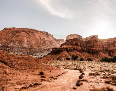 Rocks edge a red colored dirt path leading to a glowing canyon