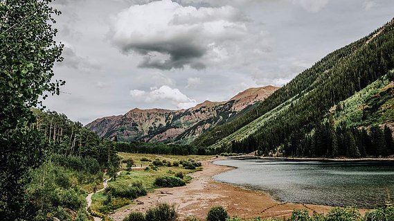 View of mountains and a lake from a trail in the trees.