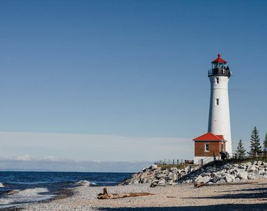 Blue waves crashing on Lake Superior where a lighthouse stands tall on the Michigan coast