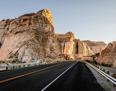 Black paved road lined with rails leading to a warm sunlit desert mountain