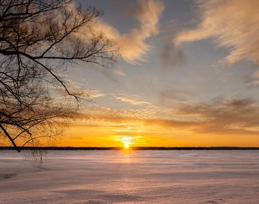 The warm sun bursts over the snow covered lake a vibrant yellow and orange