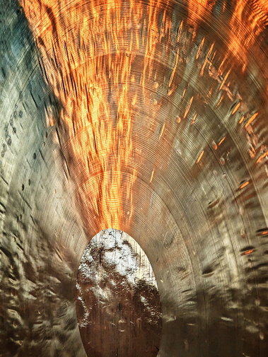 Close up of a wind gong. Light reflects upon its surface.