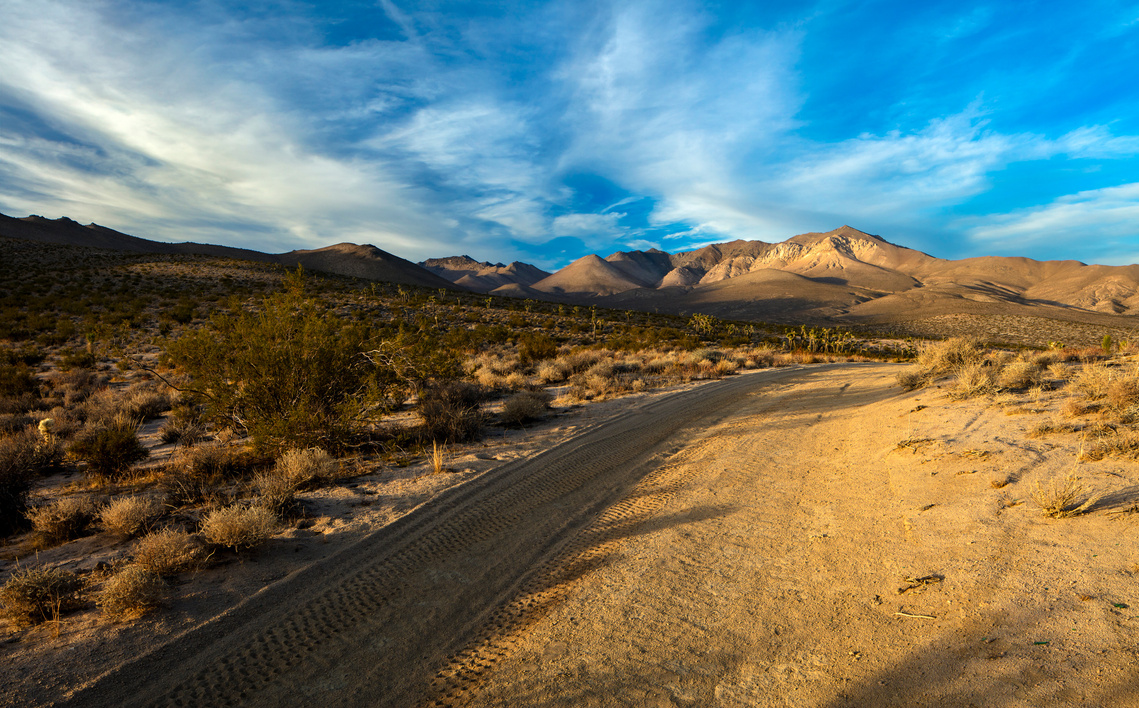 Desert road, with blue sky and clouds, traveling through California's High Mojave Desert.