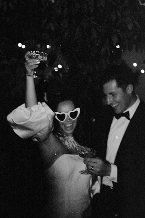 a black and white photo of a bride and groom celebrating and laughing on their wedding day. this photo is documentary-style and shot on film 